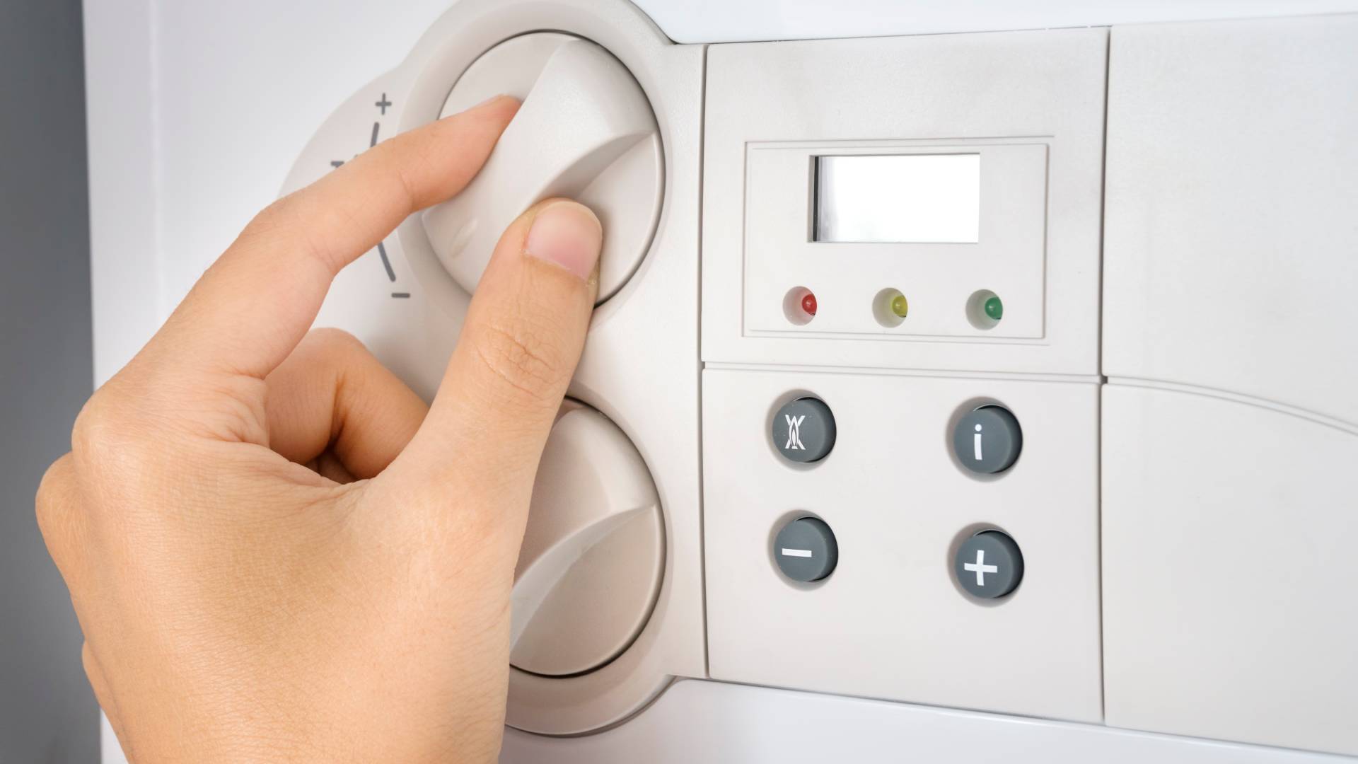 Hand adjusting temperature control dial on domestic boiler control panel