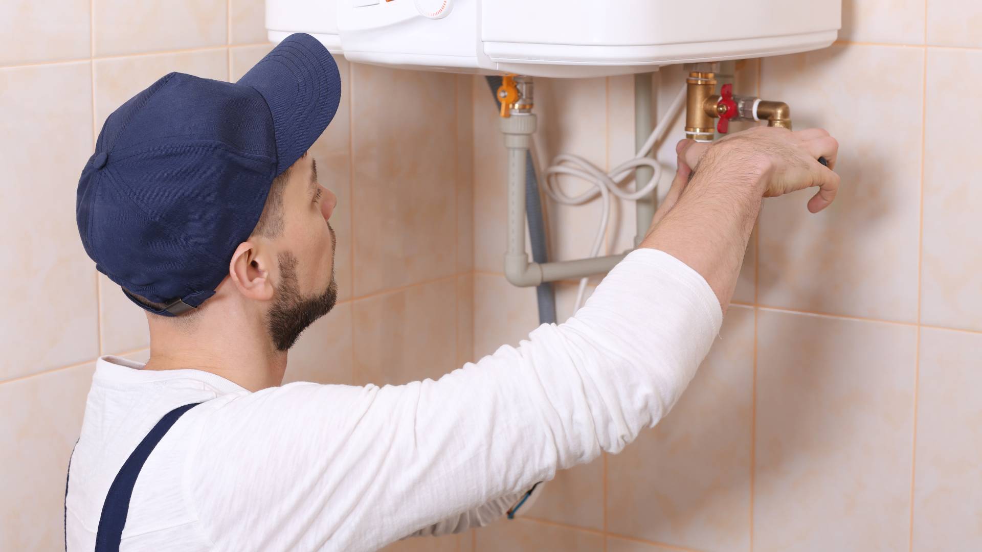 Heating engineer adjusting pipework and valve connections beneath wall mounted boiler during servicing