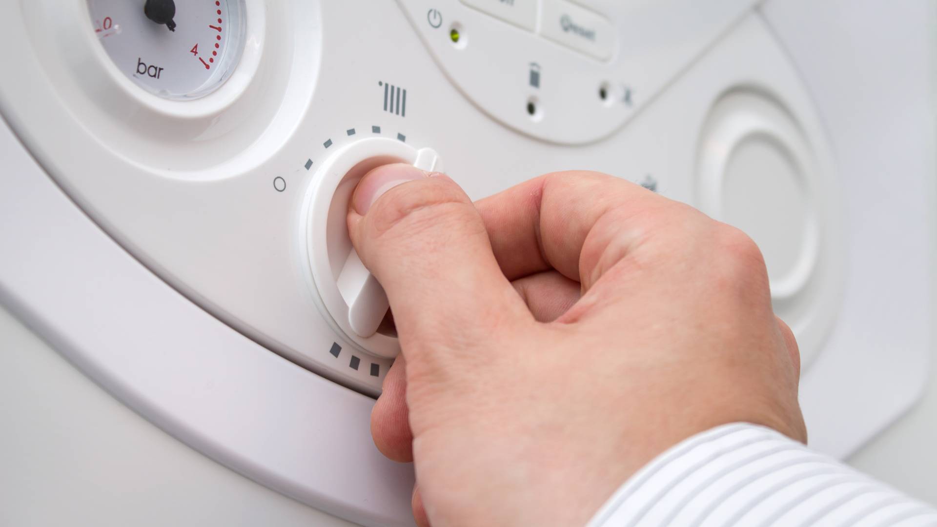 AdobeStock_91678168 Hand adjusting heating control dial on domestic boiler panel with pressure gauge visible