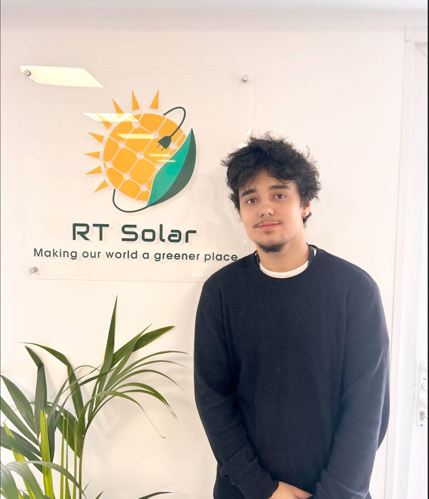 Gabriel-RT-Solar (1) RT Solar team member standing in company office beside solar energy logo sign
