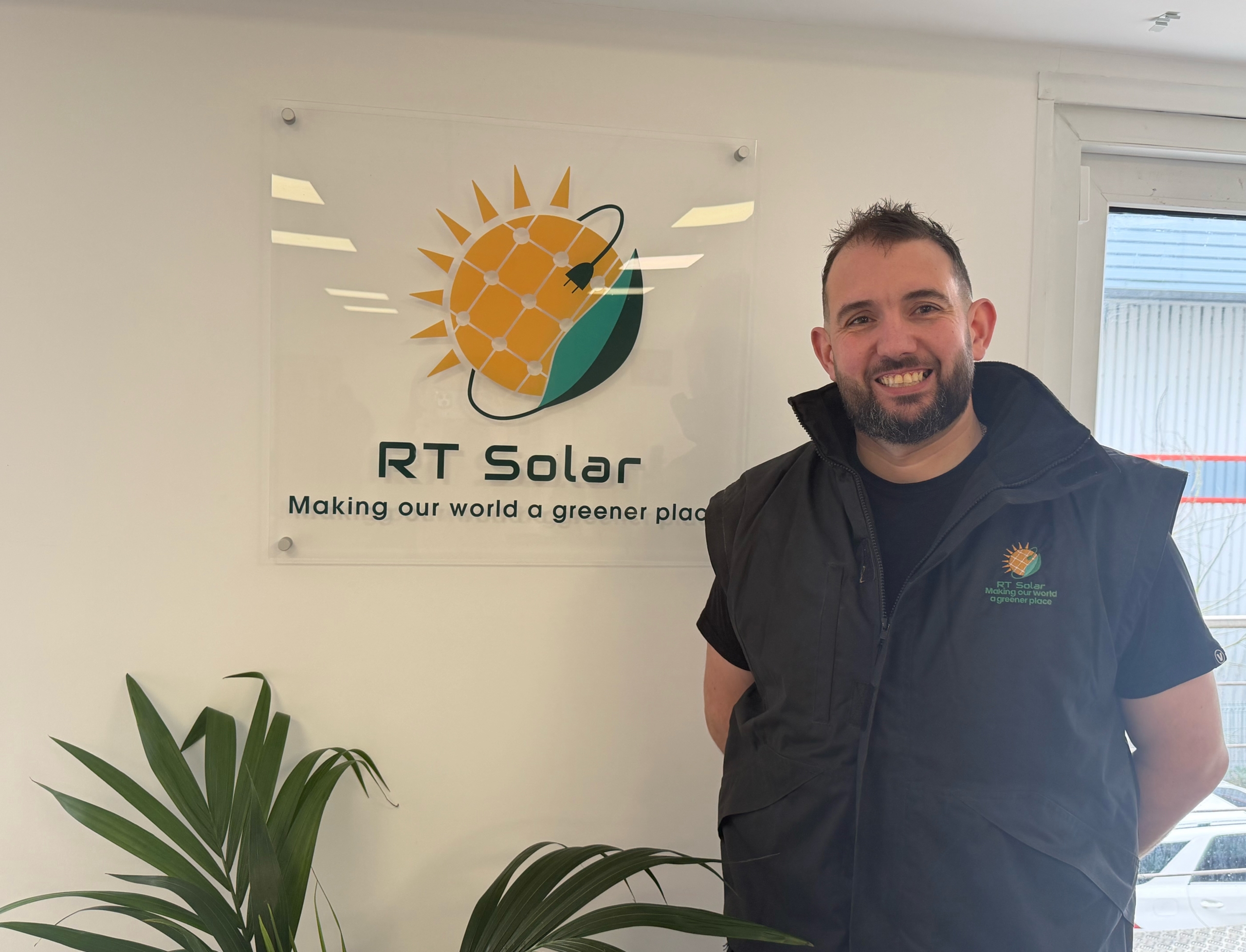 RT Solar installation manager standing in office beside company renewable energy logo sign