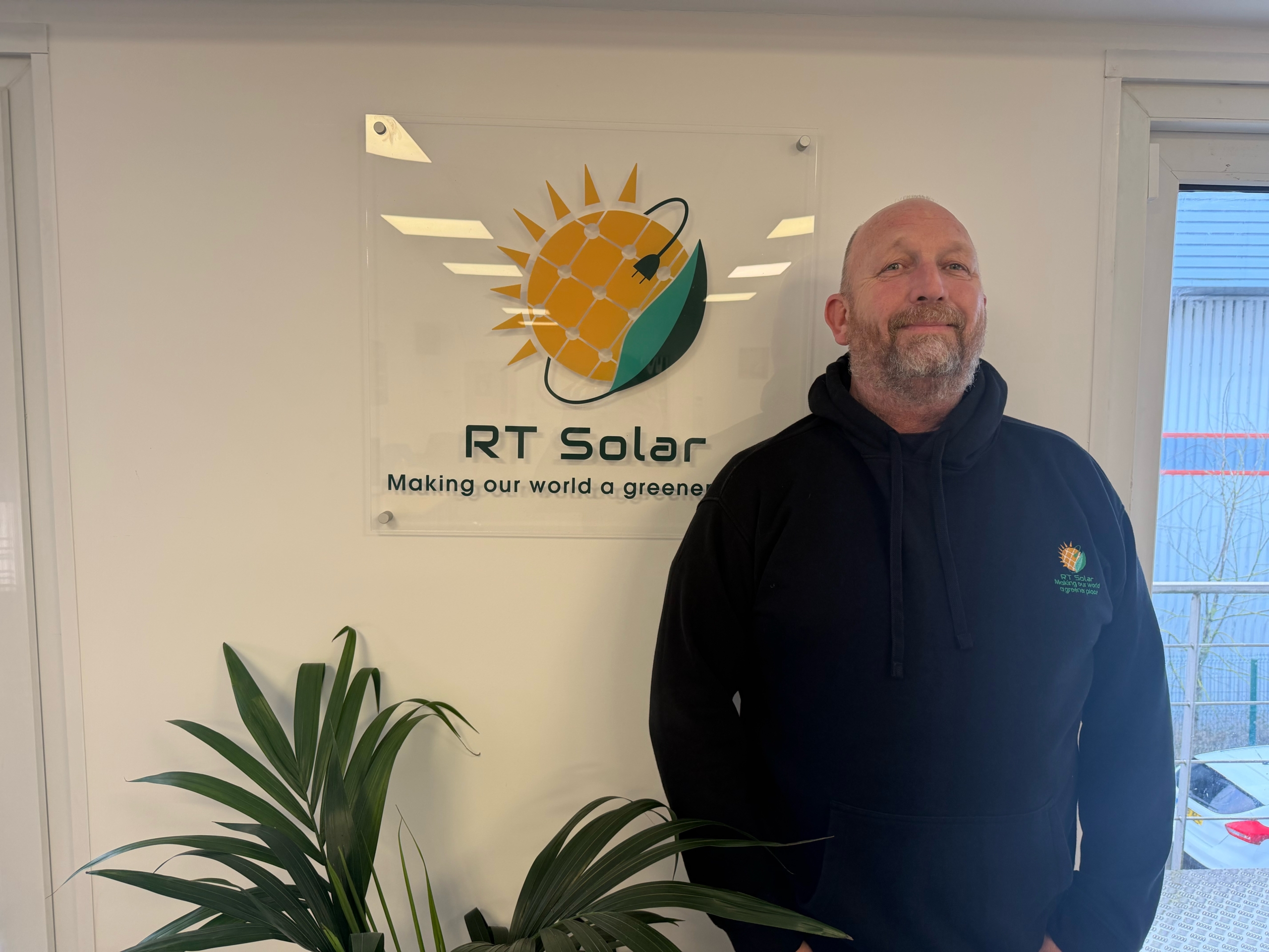 IMG_0479 RT Solar team member standing in office beside company solar energy logo sign