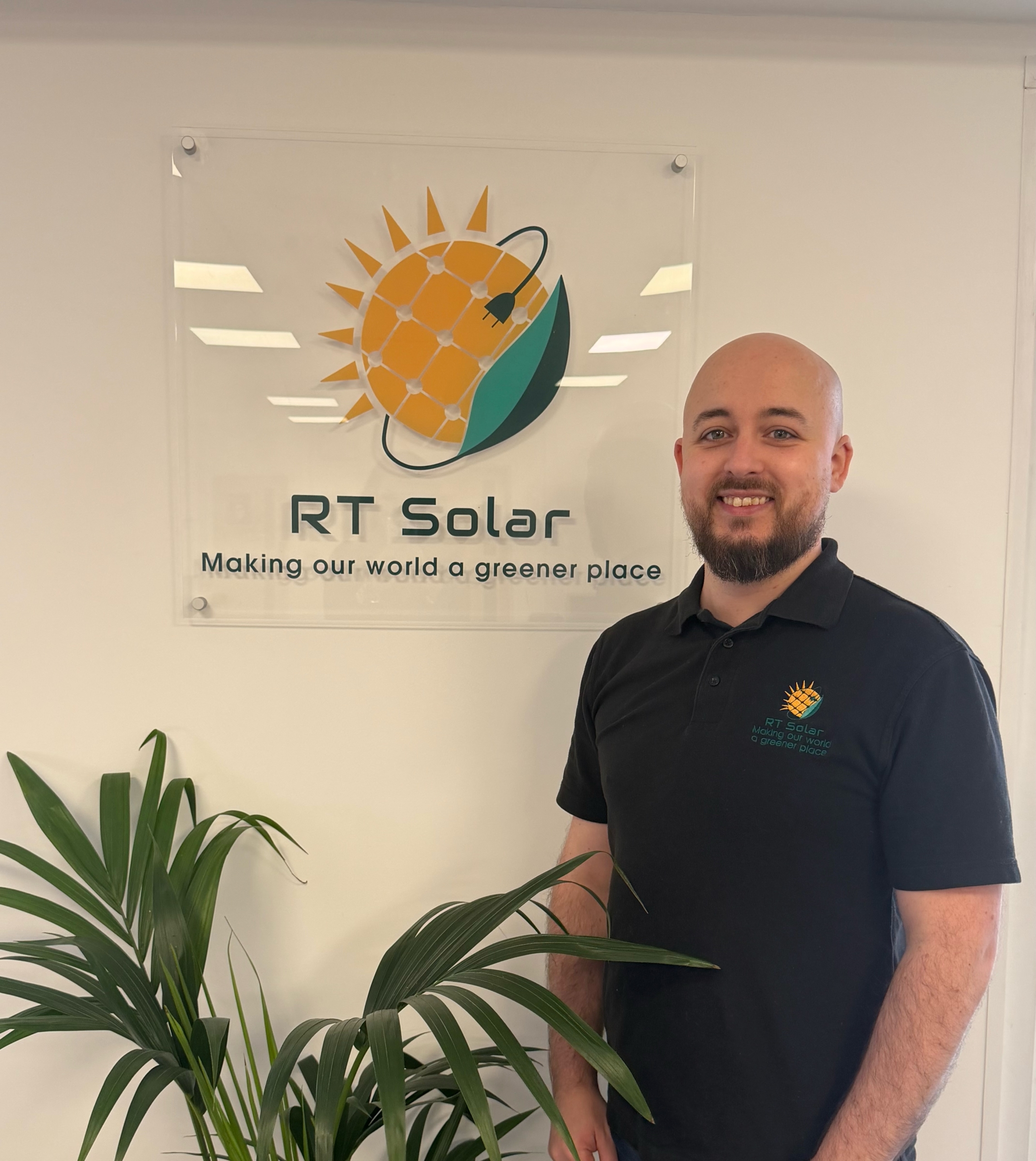IMG_0490 RT Solar team member standing in company office beside solar panel and battery storage logo sign