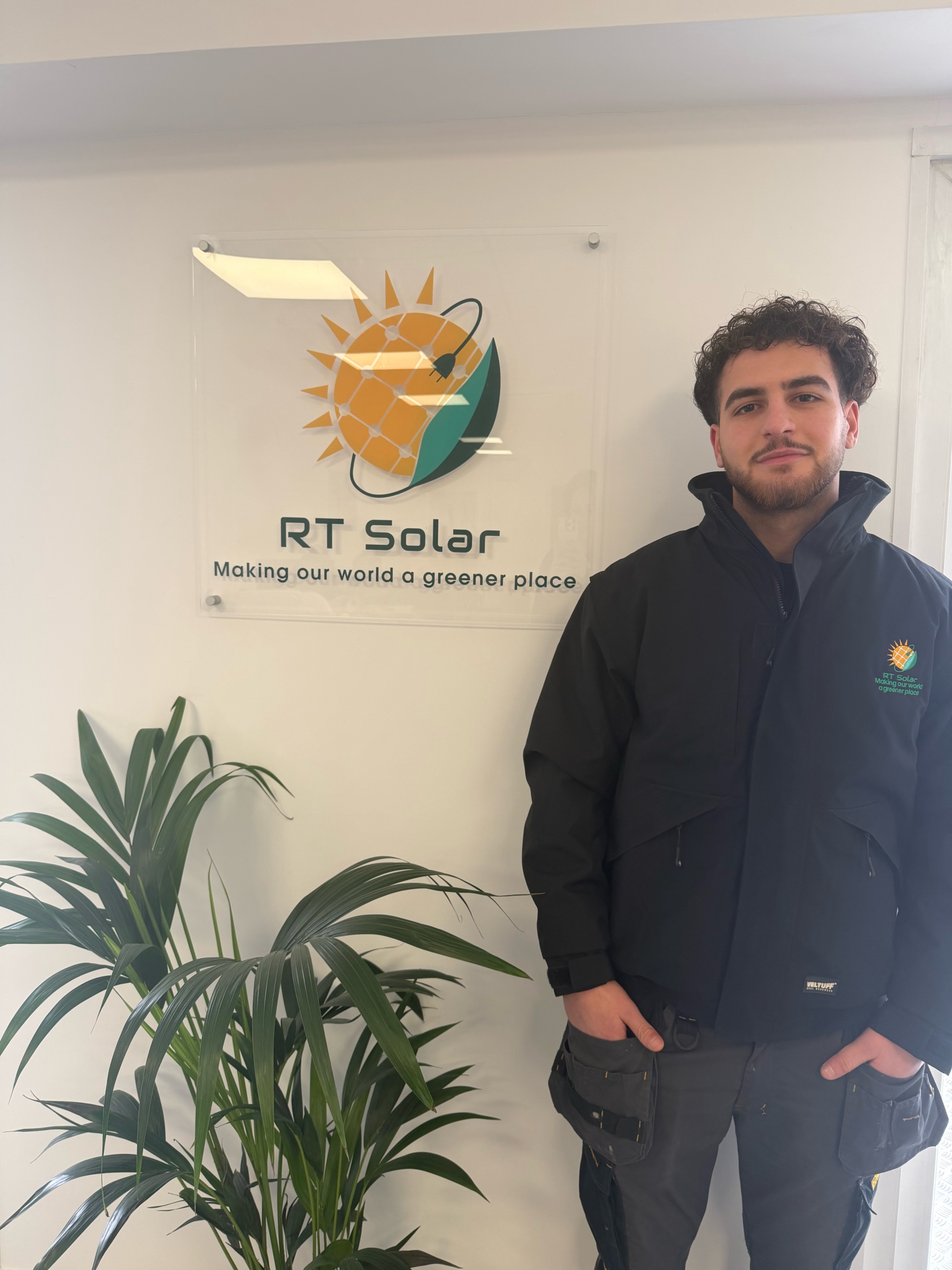 RT Solar team member standing in office beside company solar energy logo sign