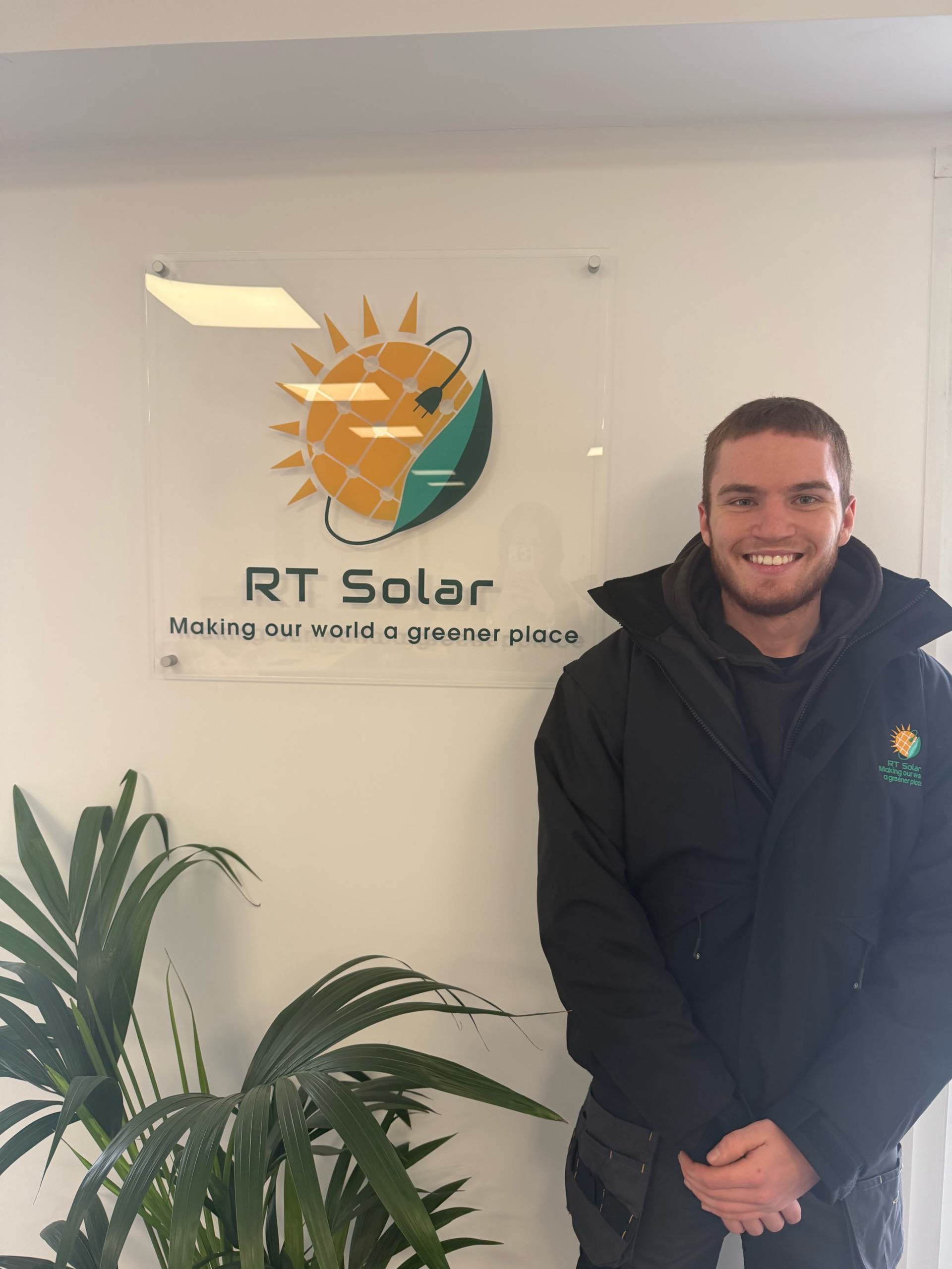 RT Solar installer standing in company office beside branded solar energy logo sign