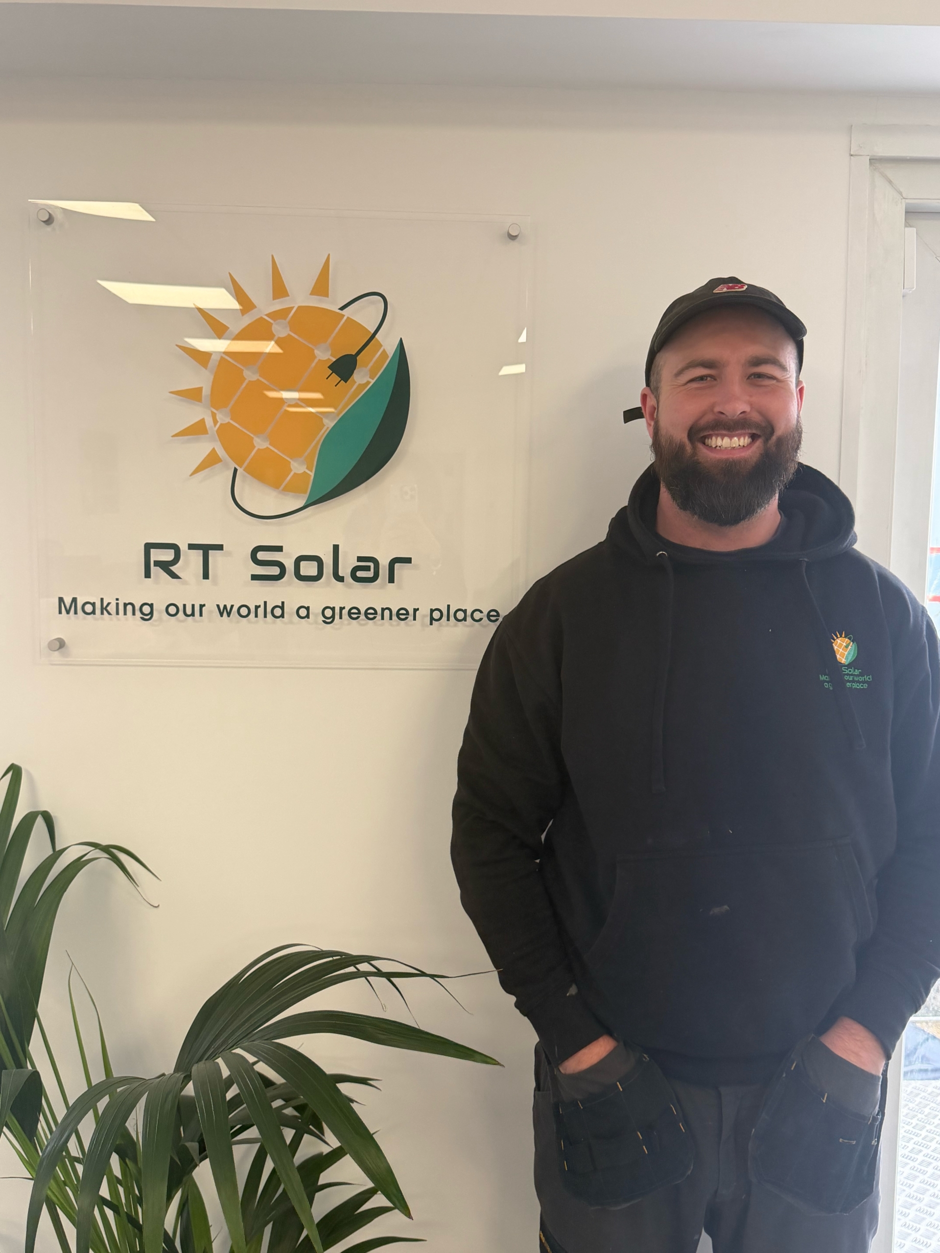 RT Solar engineer standing in company office beside branded renewable energy logo sign