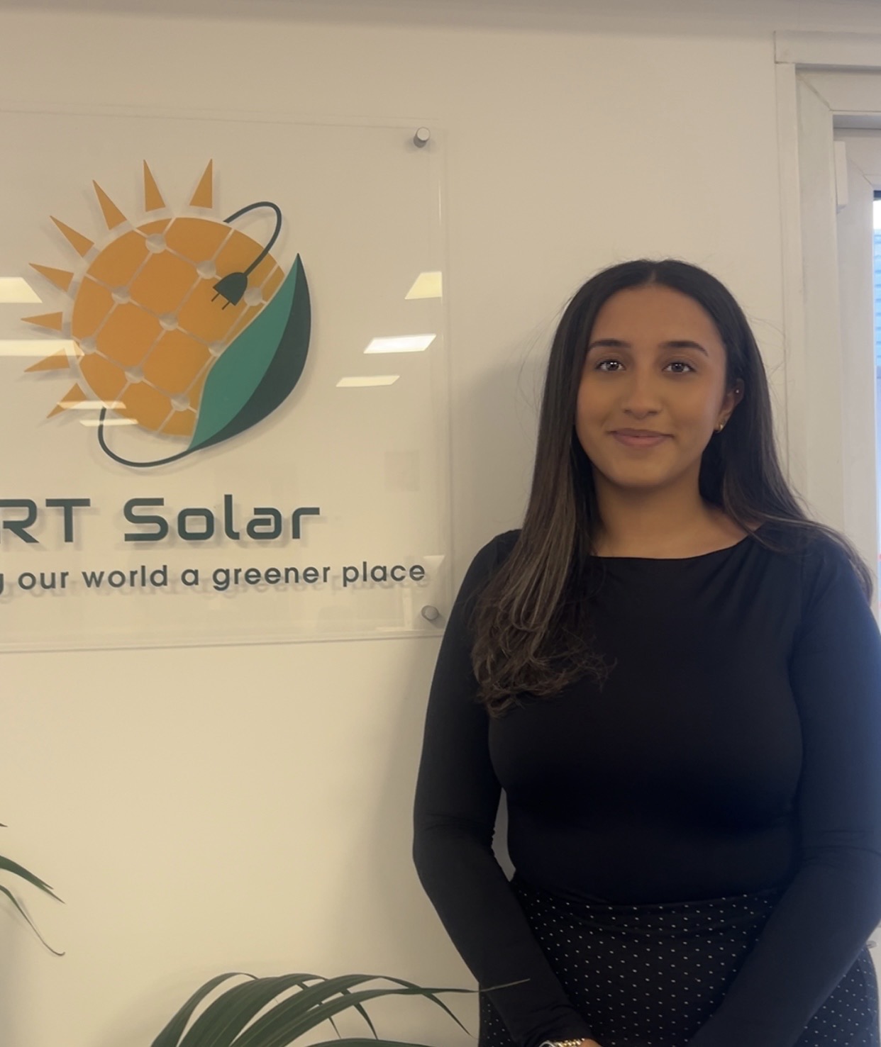 RT Solar team member standing in company office beside branded solar energy logo sign