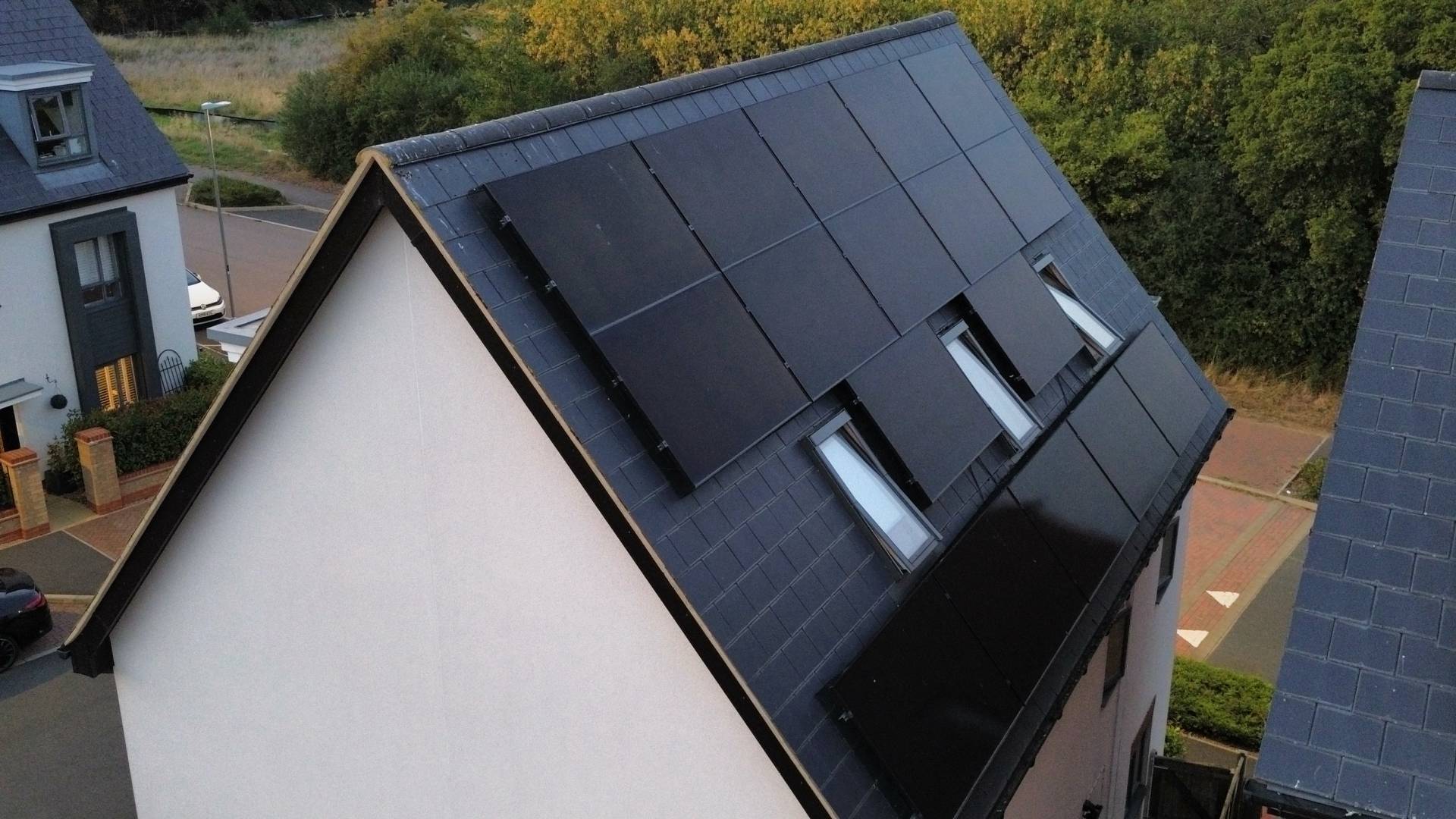 Black in-roof solar panel system on slate pitched roof with three rooflights on modern detached house at dusk