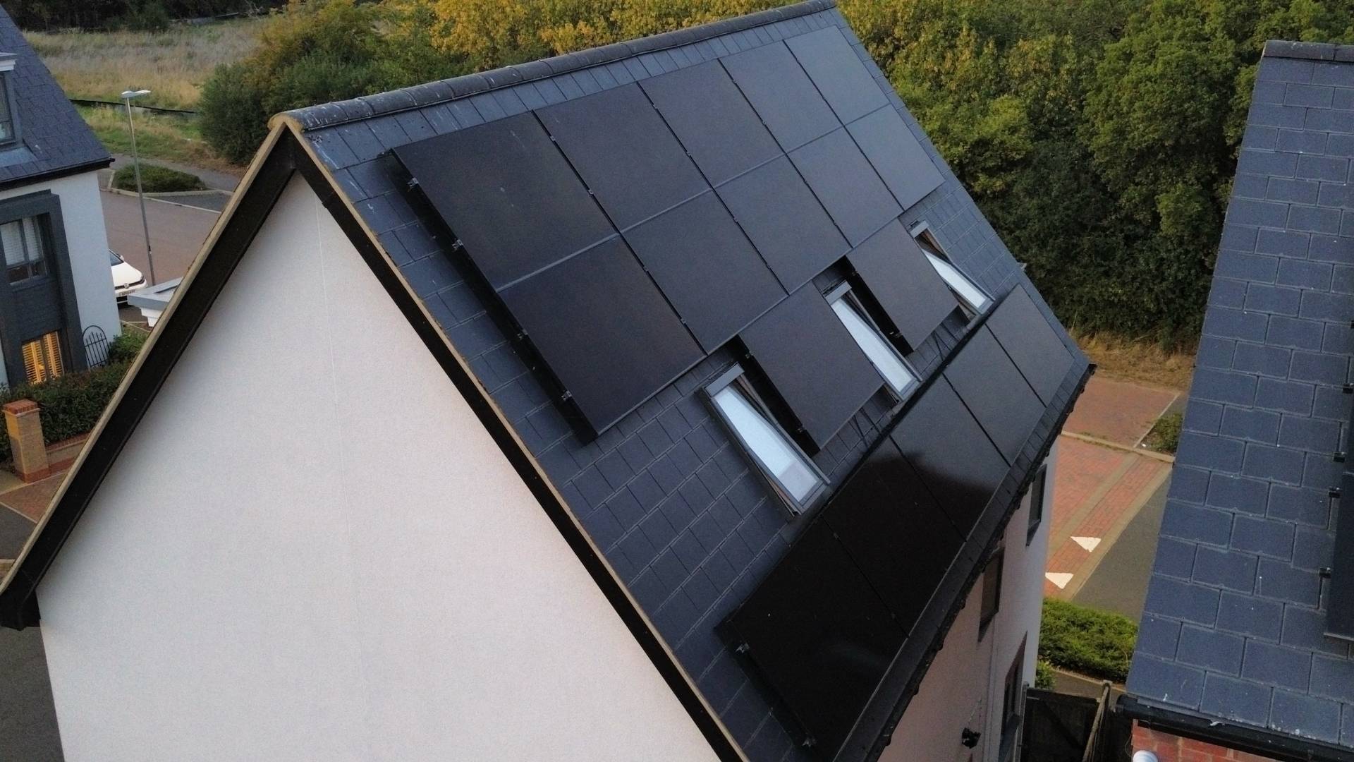 Black in-roof solar panel array on modern pitched slate roof with three roof windows in residential area