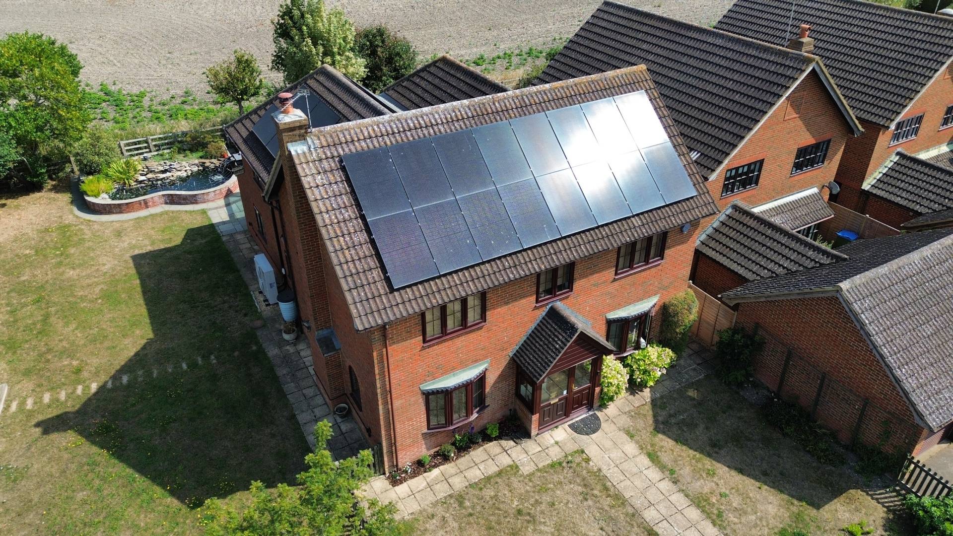 Aerial view of a detached brick house with roof-mounted solar panels installed on a pitched tiled roof in a residential area